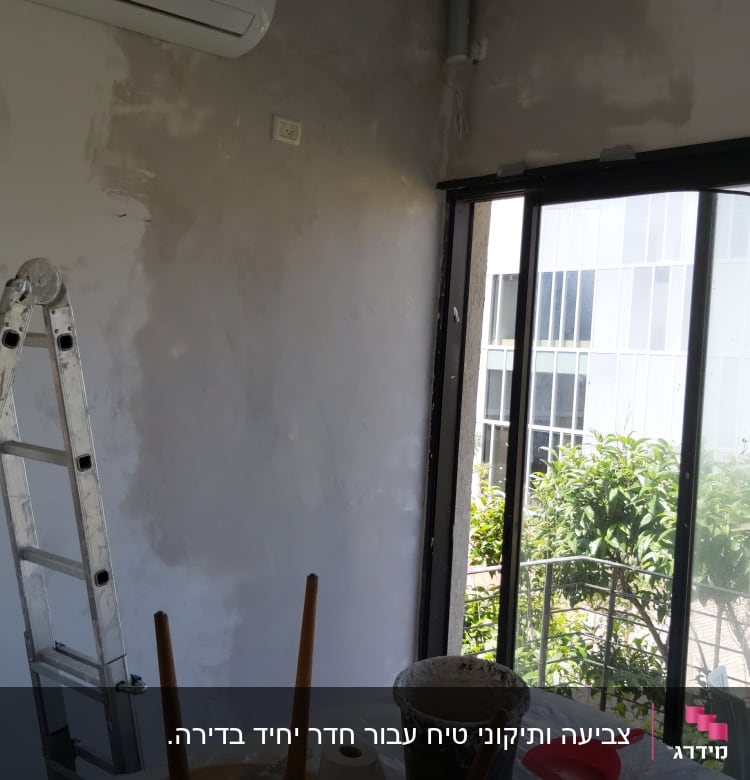 קיר צבוע חלקית עם סולם ודלי צבע